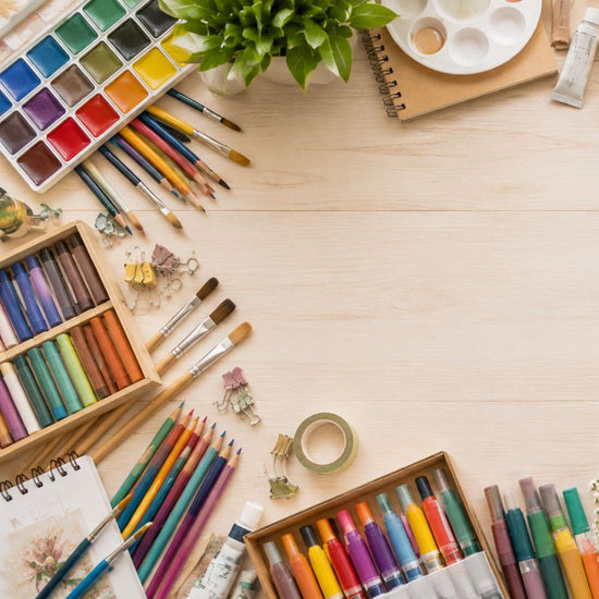 A top-down view of a light wood desk styled with various art supplies, including a watercolor palette, paintbrushes, colored pencils, markers, a notebook, and a small potted plant.